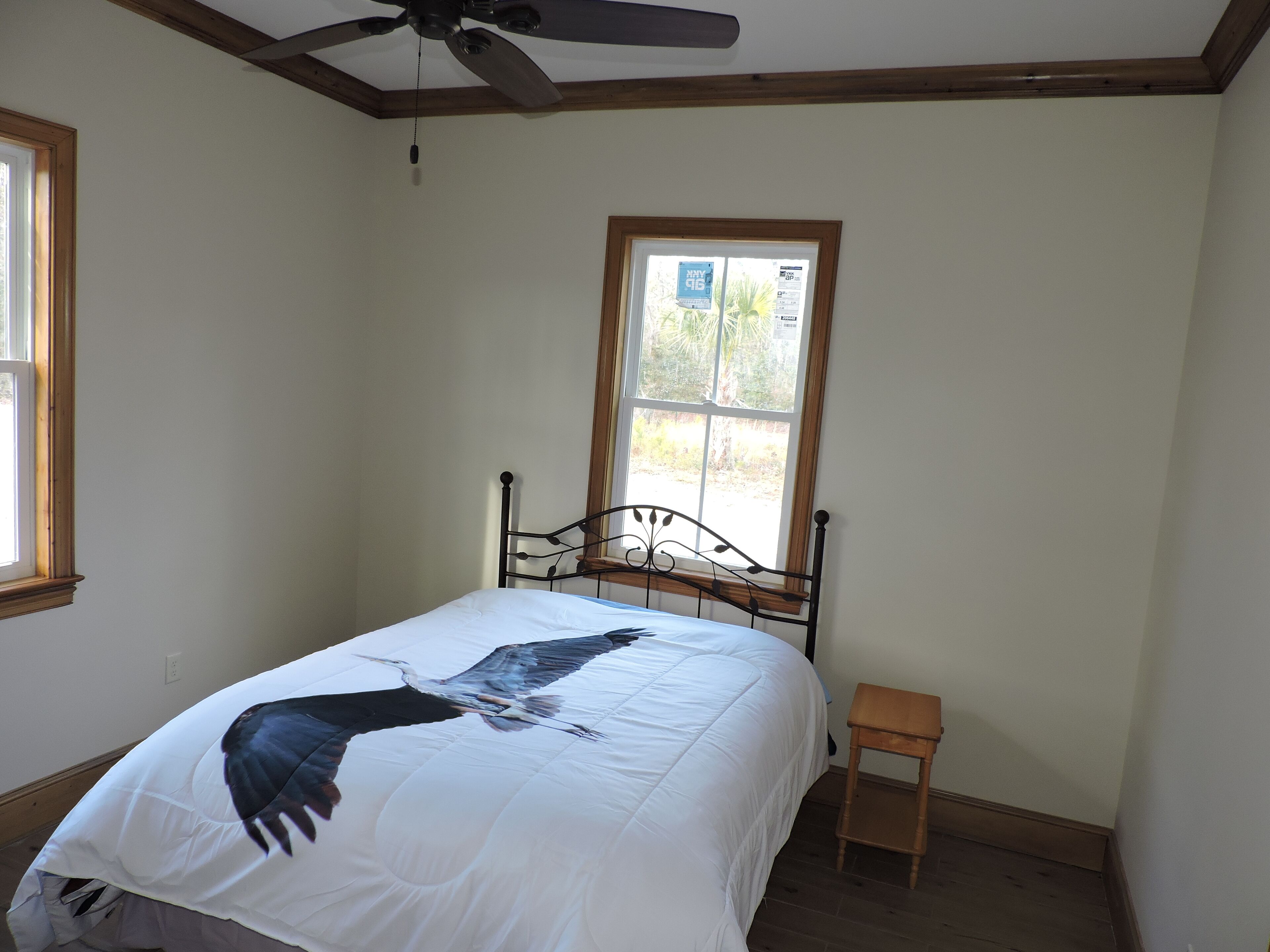 A bedroom with a bed, a window, a ceiling fan, and a small wooden stool.