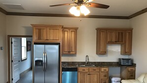 A kitchen with wooden cabinets, a stainless steel refrigerator, a dishwasher, a ceiling fan, and a toaster. - Harris Neck National Wildlife Refuge Cabin - Suite B (Townsend)