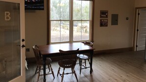 A dining area with a wooden table and chairs, a large window with a view of the outdoors, a ceiling fan, and a television mounted on the wall. - Harris Neck National Wildlife Refuge Cabin - Suite B (Townsend)