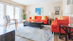 Uma sala de estar moderna com um sofá vermelho, uma cadeira de madeira, uma mesa de centro e uma janela grande com cortinas.