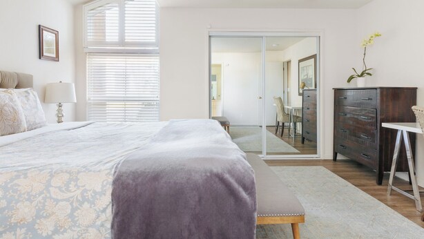 Um quarto com cama, mesa de cabeceira, abajur e cômoda.