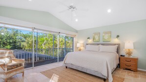 Une chambre dotée d’une grande porte-fenêtre coulissante donnant sur un balcon, d’un lit avec une tête de lit, de deux tables de chevet avec des lampes et d’un ventilateur de plafond.