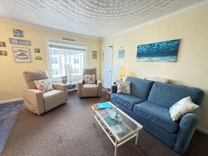 Een woonkamer met twee fauteuils, een blauwe bank, een glazen salontafel en een groot raam.