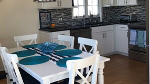 Une cuisine moderne avec des meubles blancs, un plan de travail noir et un coin repas comprenant une table et des chaises blanches.