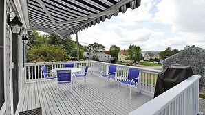 Une terrasse couverte avec une balustrade blanche, des chaises bleues et un barbecue.