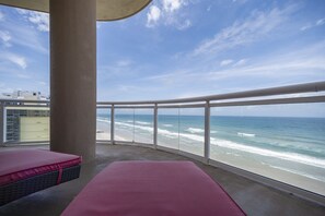 Varanda com vista para o oceano, com duas áreas de estar com assentos vermelhos e guarda-corpo de vidro.