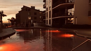 Una piscina con vista al atardecer, rodeada de edificios con balcones y una palmera.