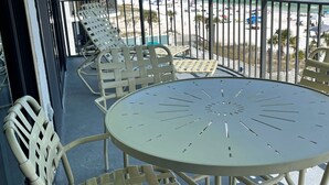 Un balcón con una mesa redonda y sillas, con vista a una playa con sombrillas y gente.