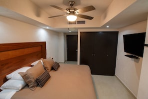 A bedroom with a bed, pillows, a ceiling fan, a TV, and a wardrobe.