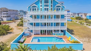 A multi-story building with a pool, outdoor seating, and a view of the surrounding area. - Premier Oceanfront Dog Friendly with Pool, Hot Tub, Elevator, Theater, Tiki Bar (Salvo)