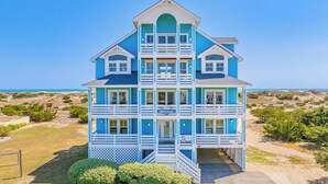 A multi-story beachfront house with balconies, a covered front porch, and a sign indicating 'Moonshine.' - Premier Oceanfront Dog Friendly with Pool, Hot Tub, Elevator, Theater, Tiki Bar (Salvo)