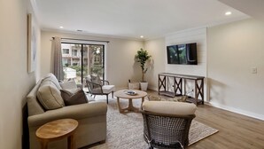 A modern living room with a sofa, chairs, a coffee table, and a TV mounted on the wall. - Courtside 61- Updated Flat - Pool View - Free Tennis (Hilton Head Island)