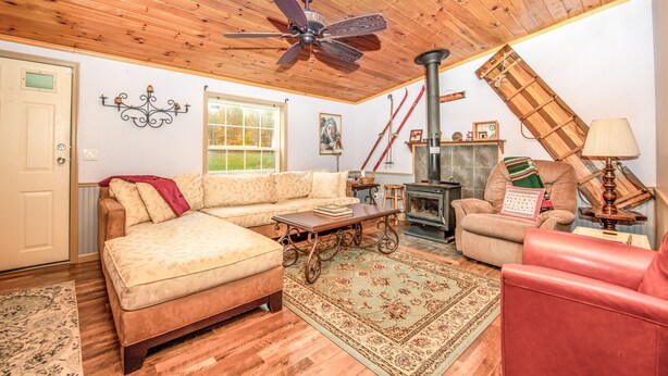 A cozy living room with a wooden ceiling, a sofa, a red chair, a fireplace, and a ceiling fan. - Check our Reviews! Spectacular Views! King bed! Upgraded Baths n Kitchen! (Hunter)