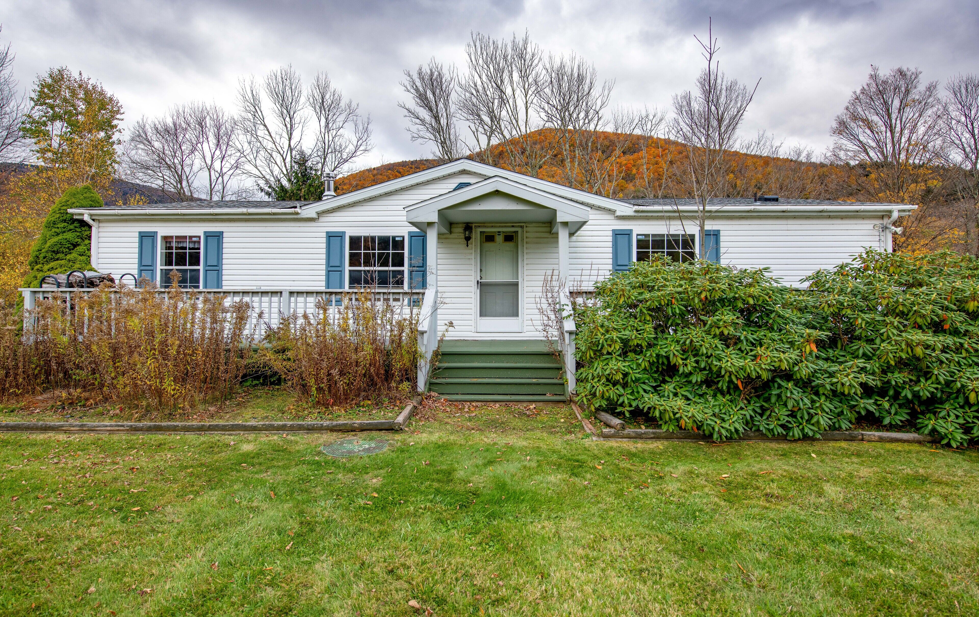 A single-story house with a front porch, a small front yard, and a hill in the background.