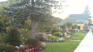 A residential area with a well-maintained lawn, flowering plants, a large tree, and a house with a yellow exterior. - Check our Reviews! Spectacular Views! King bed! Upgraded Baths n Kitchen! (Hunter)