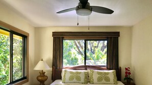 A bedroom with a bed, a nightstand, a lamp, a ceiling fan, and a window with curtains. - Spacious remodeled town home, beach access,quiet prime location in Princeville (princeville)