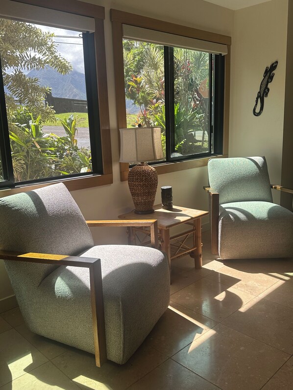 A room with two armchairs, a small table, a lamp, and a view of greenery outside.