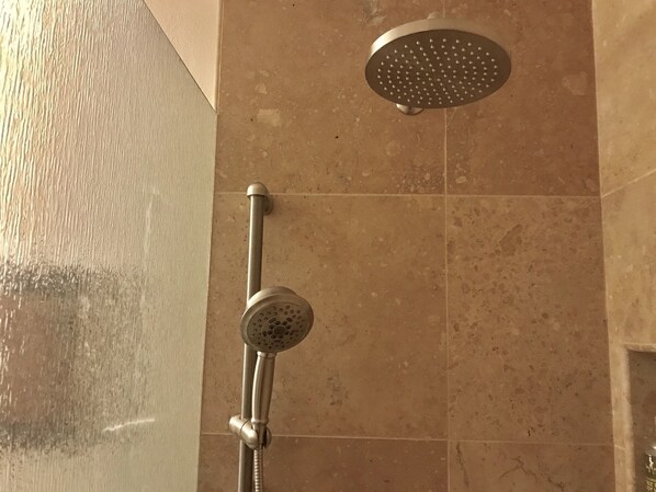 Ducha con cabezal de ducha manual y otro fijo en la pared cubierta de azulejos.