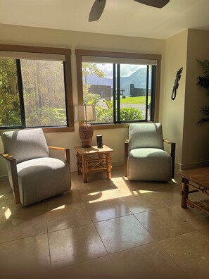 A room with two armchairs, a small table, and a view of greenery and mountains through large windows.