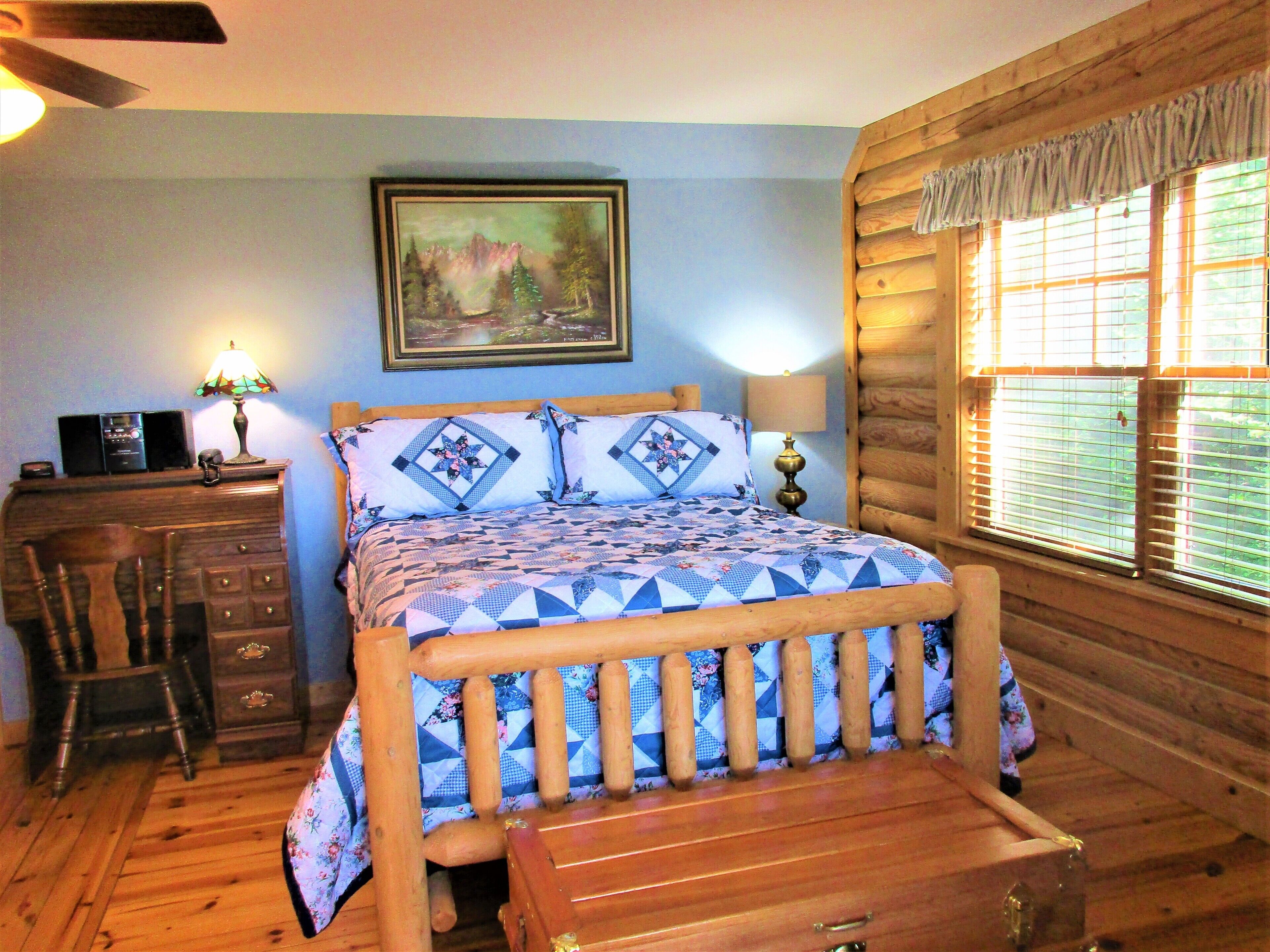 Un dormitorio de estilo cabaña de madera con una cama, cómoda y escritorio.
