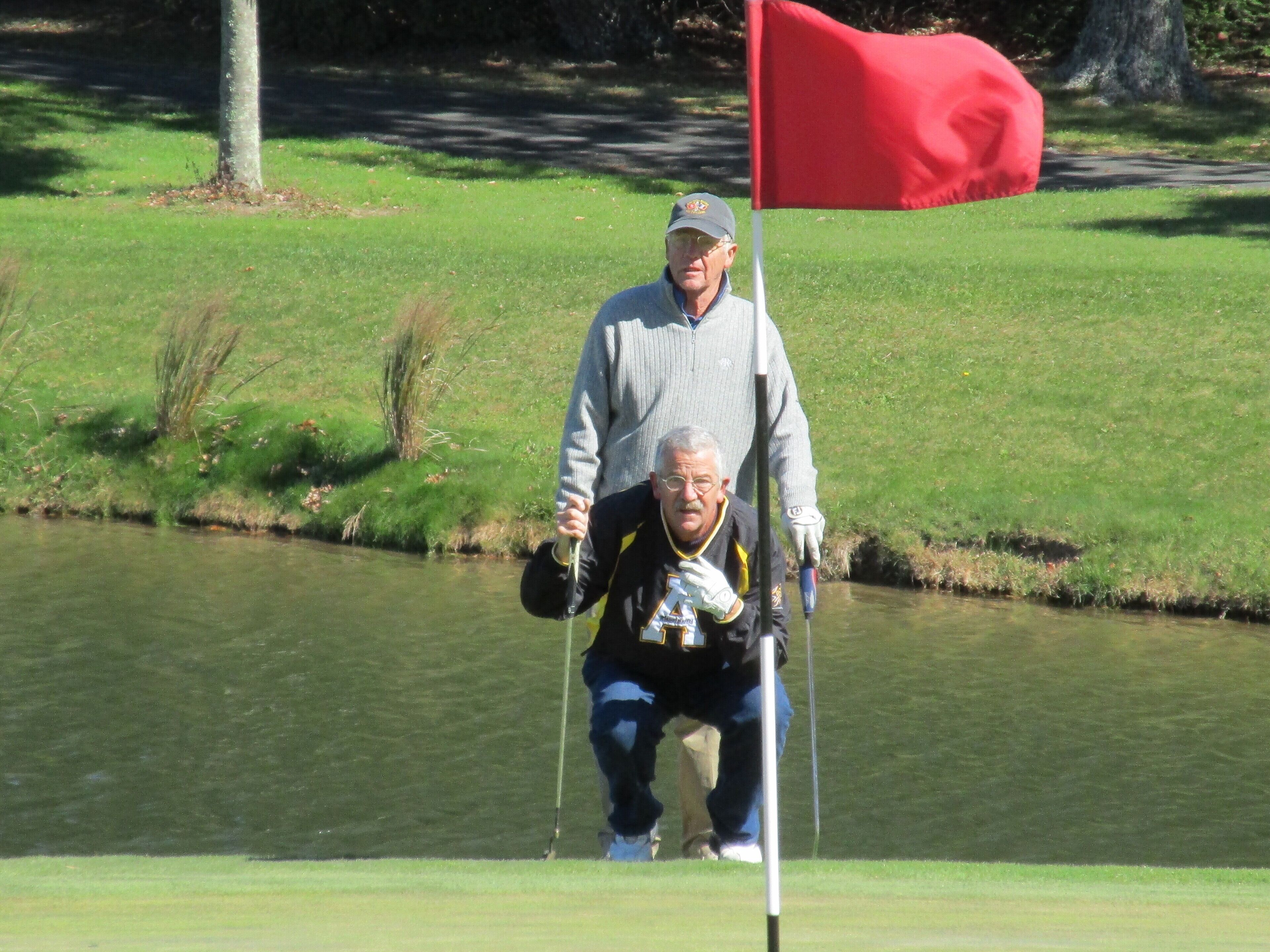 A golf course with a red flag, a pond, and a grassy area.