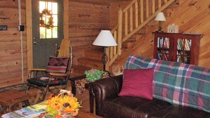 A cozy log cabin interior with a wooden staircase, a leather sofa, a plaid blanket, and a bookshelf. - ALPINE LOG CABIN/COZY, COMFORTABLE, MODERN/BLUE RIDGE MOUNTAINS NEAR BOONE N.C. (Boone)