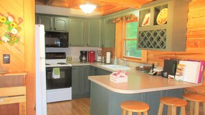 A kitchen with wooden cabinets, a refrigerator, a microwave, a stove, a sink, and two bar stools. - ALPINE LOG CABIN/COZY, COMFORTABLE, MODERN/BLUE RIDGE MOUNTAINS NEAR BOONE N.C. (Boone)