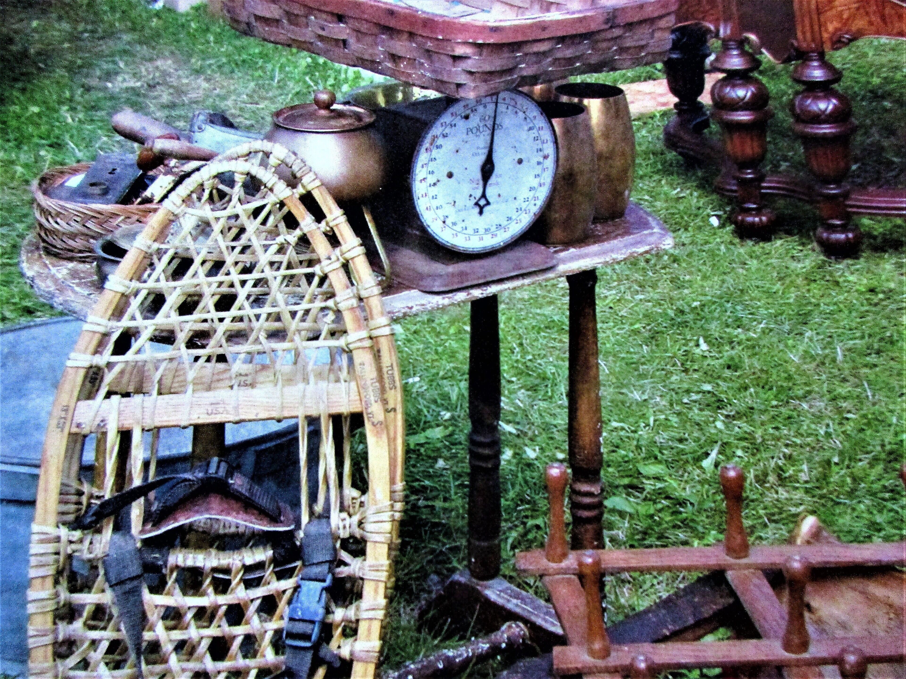 A rustic outdoor setting with a wooden table displaying various antique items including a scale, a basket, and a wheel.