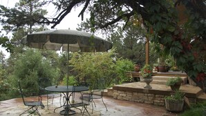 An outdoor patio with a stone table and chairs, an umbrella, and potted plants. - Beautiful home in private setting yet only15 min to town  & 10 min to lake (Durango)