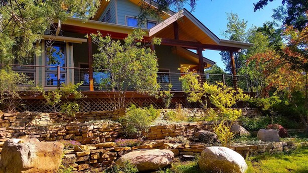 A two-story house with a wooden deck and a stone retaining wall. - Beautiful home in private setting yet only15 min to town  & 10 min to lake (Durango)
