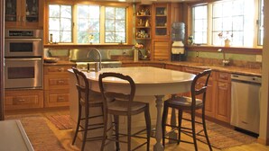 A kitchen with wooden cabinets, a central island with chairs, a built-in oven, and a window with a view of trees. - Beautiful home in private setting yet only15 min to town  & 10 min to lake (Durango)