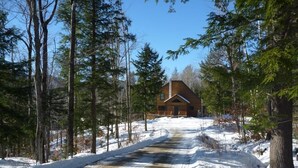 Une cabane entourée d’arbres, avec un sentier enneigé qui y mène.