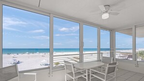 Una stanza con un'ampia finestra vista spiaggia, una ventola a soffitto e un tavolo con sedie.