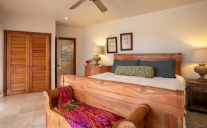 Een slaapkamer met een houten bed, twee bedlampen, een nachtkastje, een houten bankje en een plafondventilator.