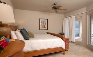 A bedroom with a wooden bed, a ceiling fan, a framed artwork, and a view through a glass door. - Mango Bay: Amazing North Shore Views! (St. John)