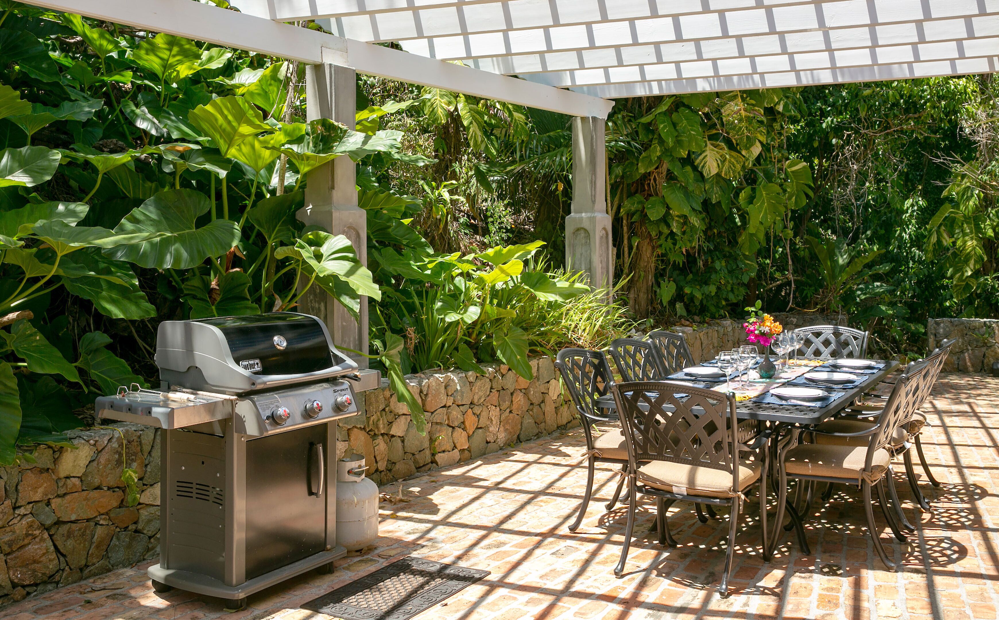 An outdoor patio with a grill, stone wall, and lush greenery.