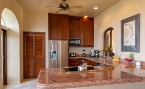 A kitchen with wooden cabinets, stainless steel appliances, granite countertops, and a ceiling fan.