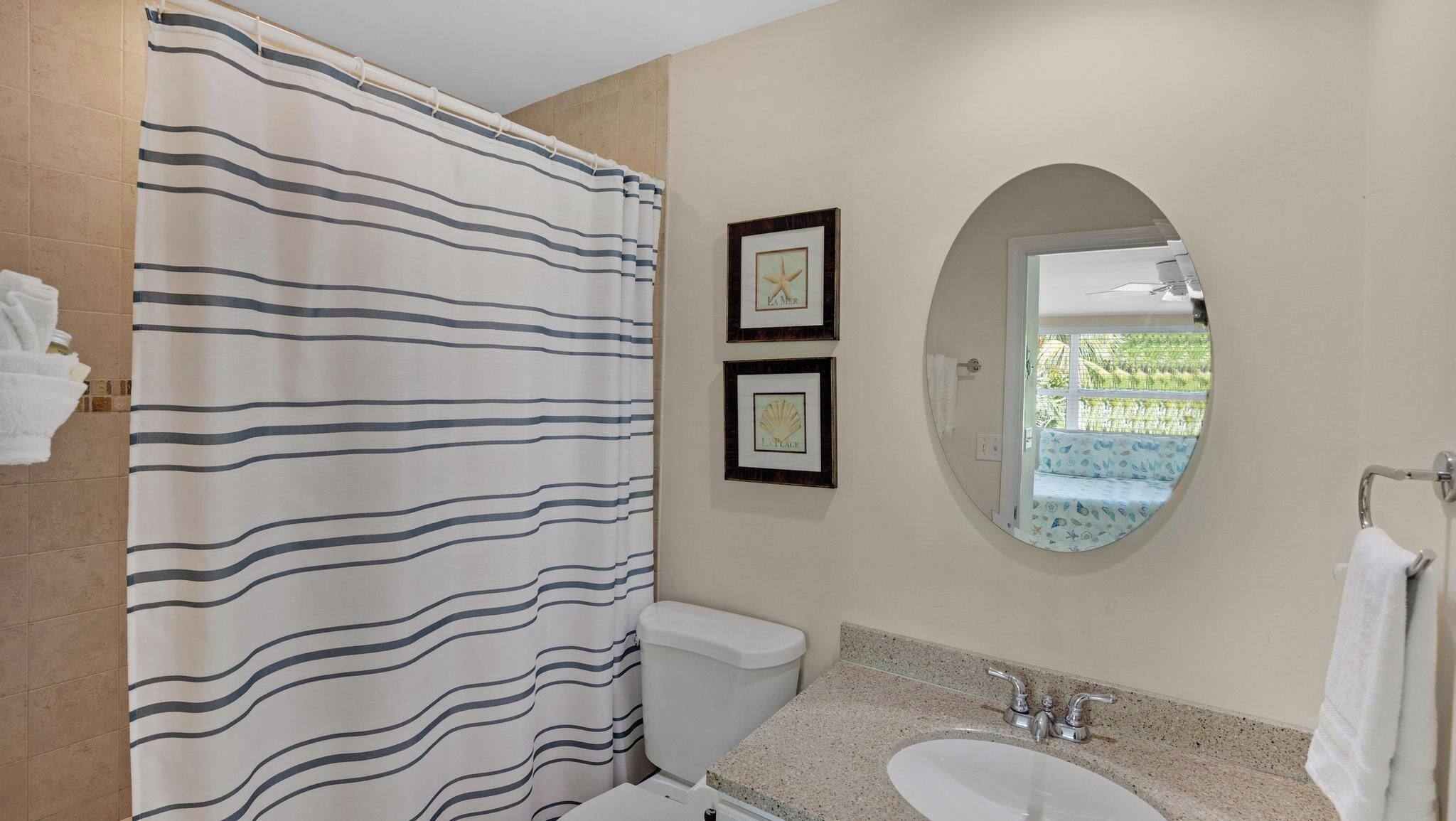 A bathroom with a striped shower curtain, a toilet, a sink with a mirror, and two framed pictures on the wall.