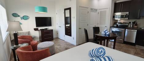 A hotel room with a bed, a TV, a desk, and a kitchenette.