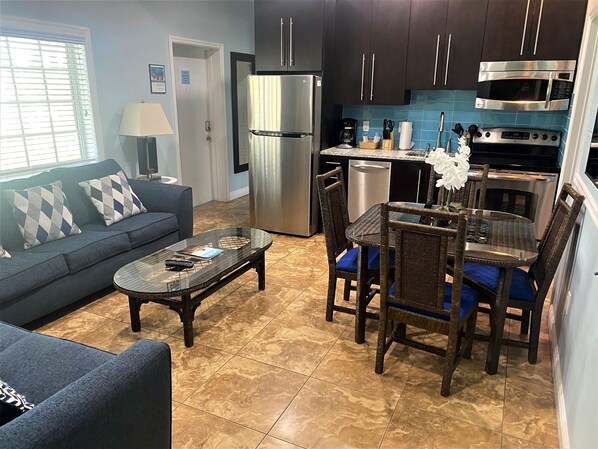 A modern kitchen with dark cabinets, stainless steel appliances, and a dining area with wicker chairs and a glass table.