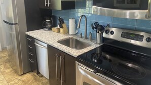 A modern kitchen with stainless steel appliances, a granite countertop, and blue backsplash tiles. - Spacious 2BR Close to World-Famous Sand Beach Club at Siesta Key #102A by RVA (Sarasota)