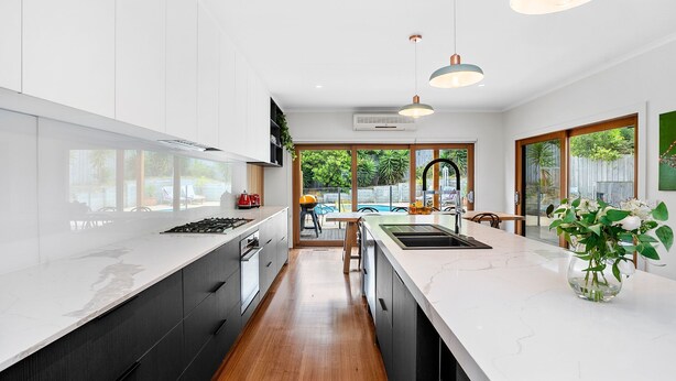A modern kitchen with white cabinets, a marble countertop, and a central island. There is a view of a pool and greenery outside. - SALTWATER POOLSIDE -8m Heated* Pool, an entertainers delight -BONUS*NIGHTS 2026 (rye)