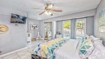 A bedroom with a bed, a ceiling fan, a TV mounted on the wall, a mirror, and a window with curtains.
