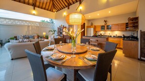 Un vaste espace de vie comprenant un coin repas avec une table ronde, des sièges confortables et une cuisine située à l’arrière-plan.