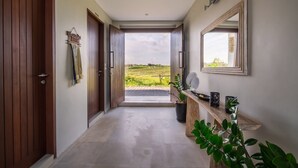 Un couloir avec des portes en bois, une plante en pot, un miroir et une vue sur un paysage verdoyant.
