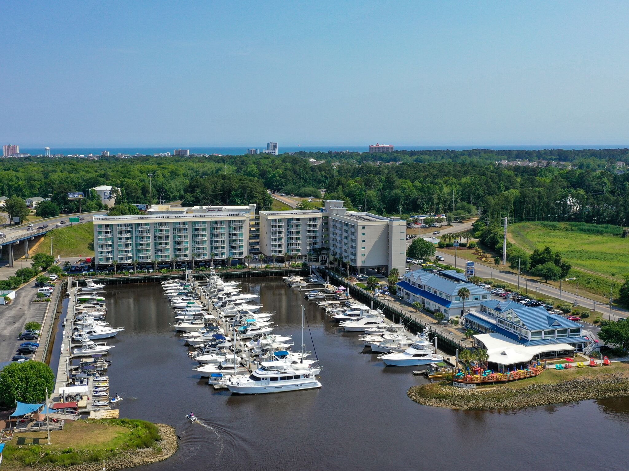 Un port de plaisance où sont amarrés de nombreux bateaux, un grand bâtiment d’hôtel et une petite île dotée d’un quai.