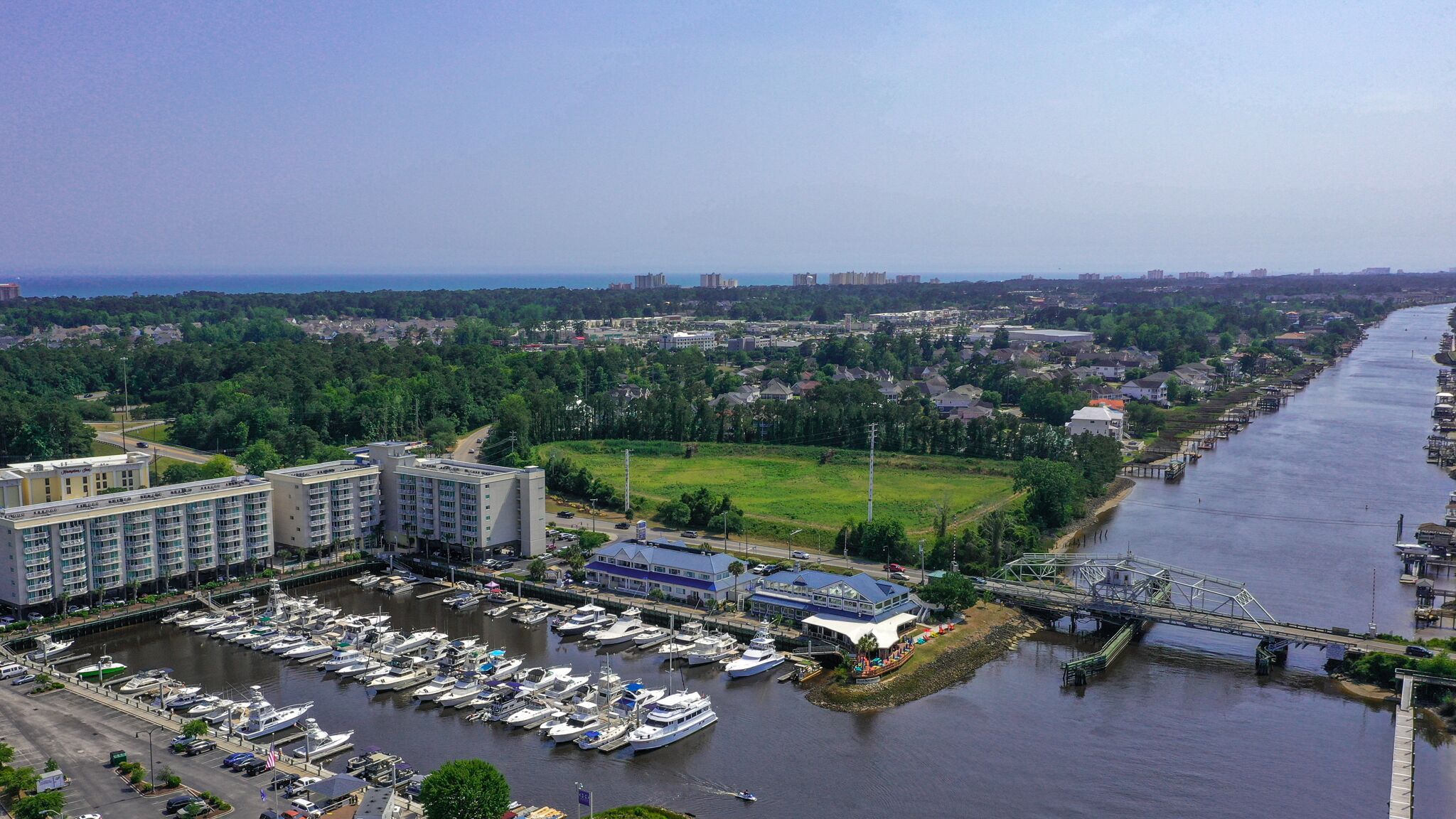 Een jachthaven met diverse boten afgemeerd, een groot hotelgebouw en een rivier met een brug.