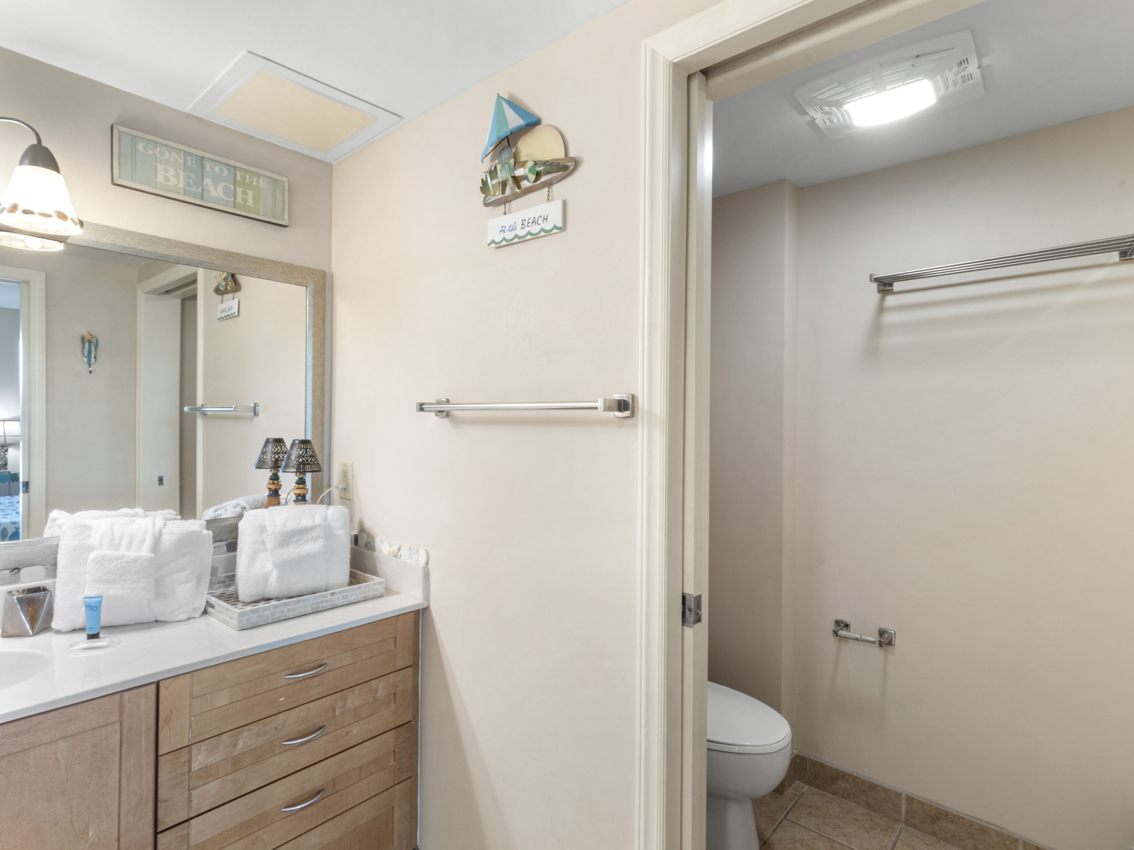 A bathroom with a toilet, a towel rack, a mirror, and a sink with toiletries.