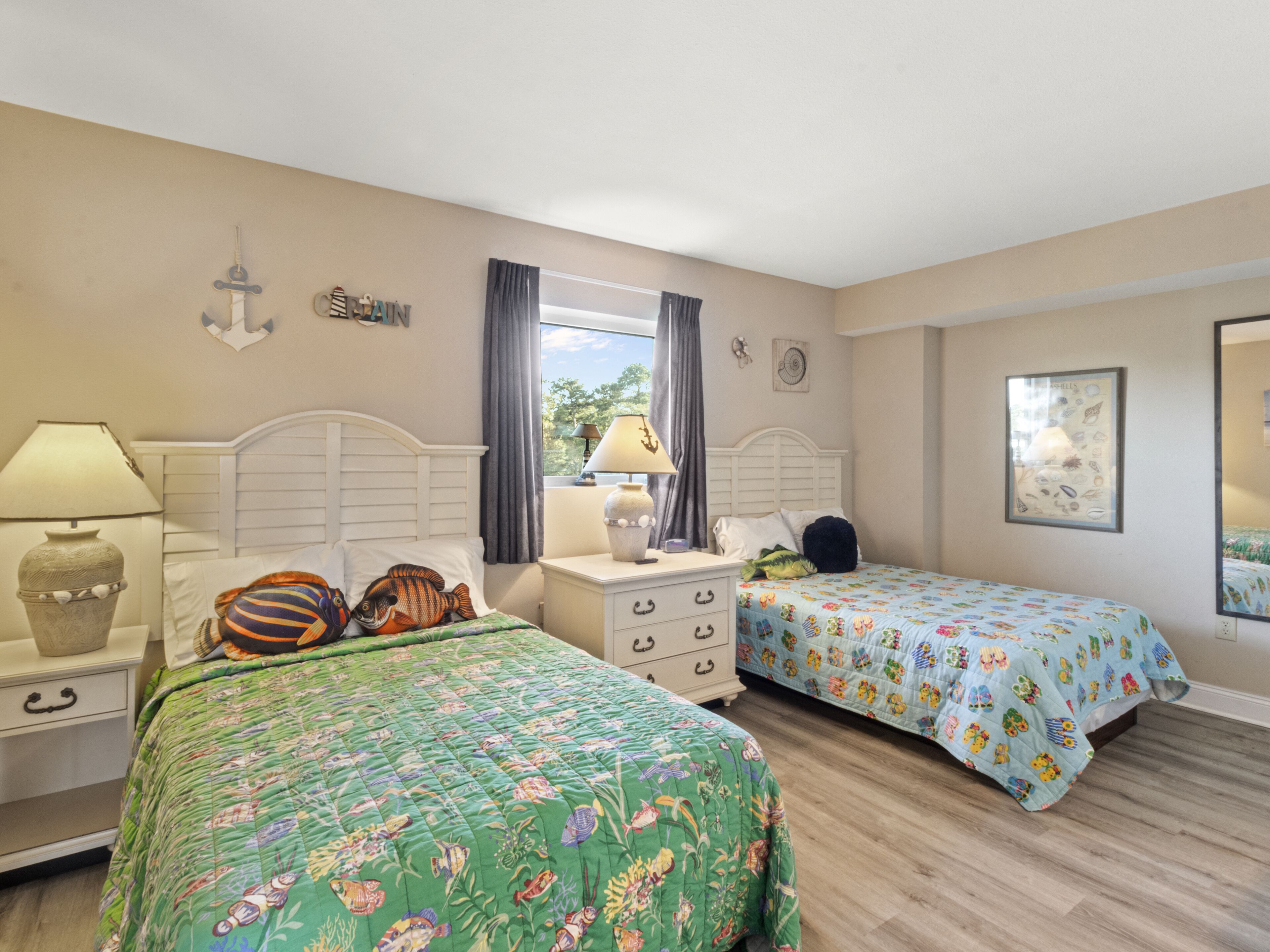 A bedroom with two beds, a nightstand, a dresser, and a window with curtains.