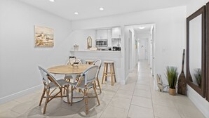 Una cocina moderna con armarios blancos, una isla central y una zona de comedor con sillas de mimbre y una mesa redonda.